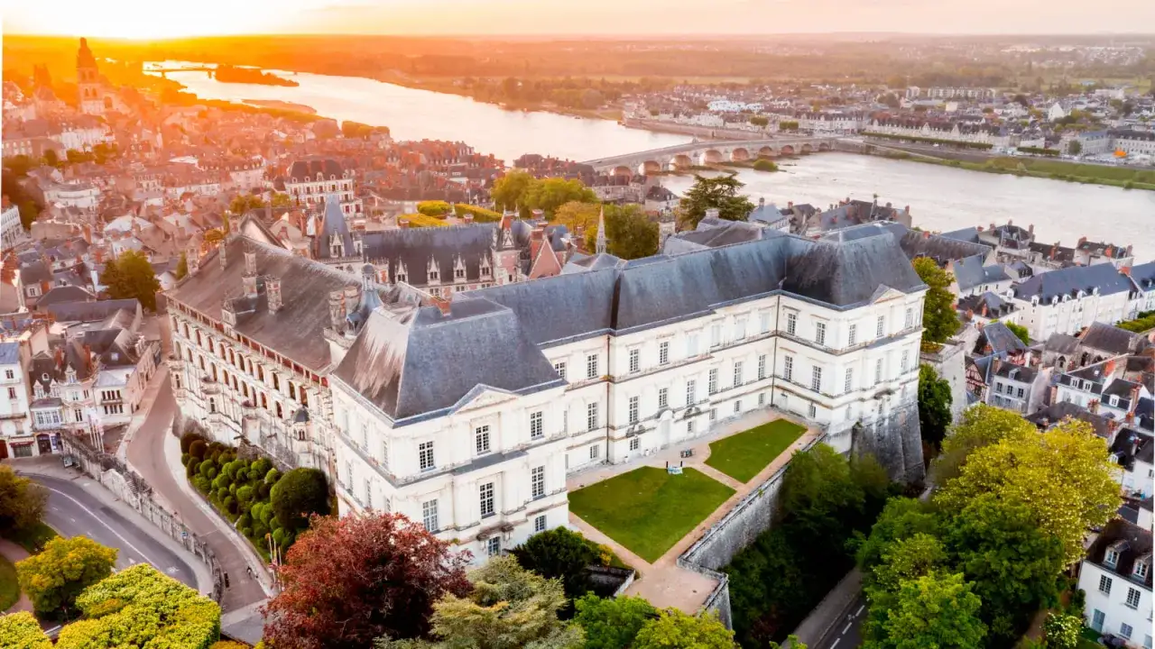 Vue a&eacute;rienne du ch&acirc;teau de Blois au coucher du soleil, avec la Loire et la ville en arri&egrave;re-plan.