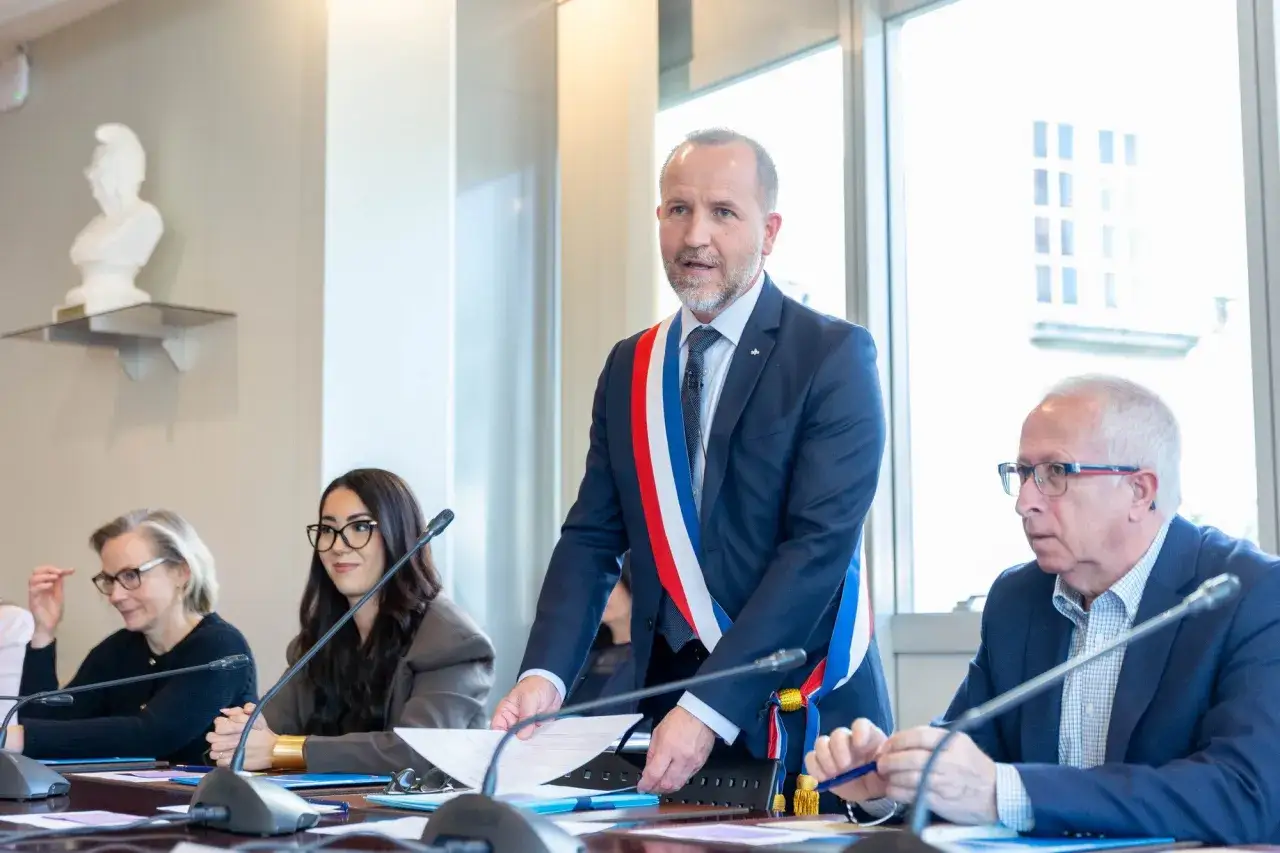 Laurent Raymond, homme politique, porte l'&eacute;charpe tricolore lors d'une r&eacute;union. Il est entour&eacute; de plusieurs personnes assises &agrave; une table.