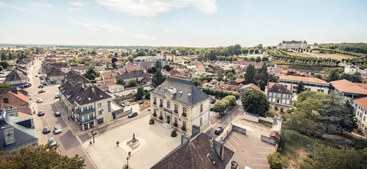 Vue aérienne de Brienne-le-Château, avec son hôtel de ville et ses toits de tuiles, sous un ciel bleu.