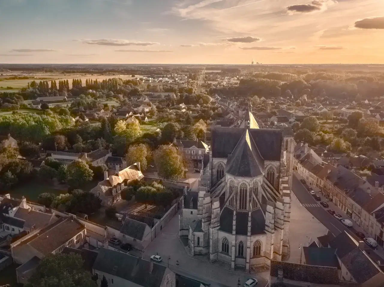 Vue a&eacute;rienne de Cl&eacute;ry-Saint-Andr&eacute; au coucher du soleil, avec sa basilique imposante au premier plan et les toits des maisons s'&eacute;tendant &agrave; perte de vue.