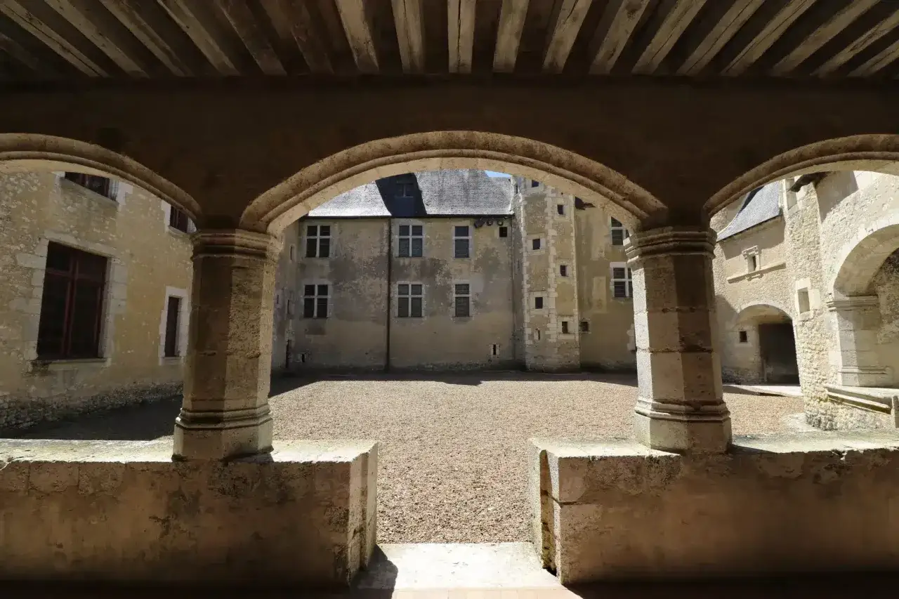 Vue d'une cour intérieure d'un château, avec des arches en pierre et un sol en gravier. Une fougère sur bièvre pourrait pousser ici, près des vieilles pierres.