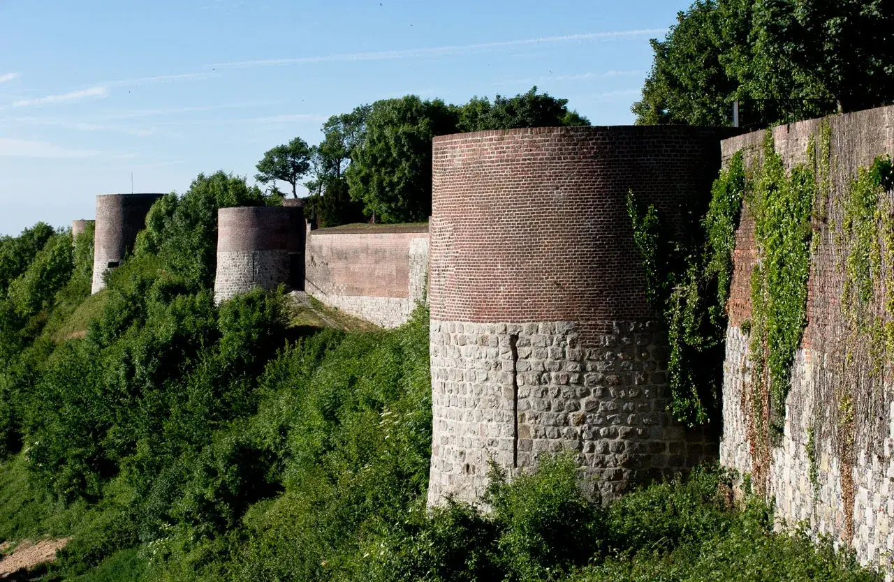 Tours circulaires en briques et pierre du château de Montreuil, bordées de verdure luxuriante sous un ciel bleu.