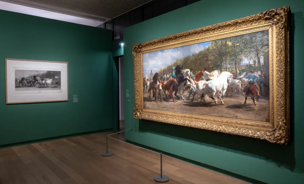 Dans un musée, une peinture de Rosa Bonheur représente des chevaux en mouvement. Une autre œuvre, plus petite, est accrochée à gauche.