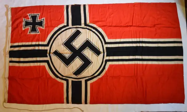 Drapeau rouge avec une croix noire et blanche dans le coin supérieur gauche et une croix gammée noire sur un cercle blanc au centre. L'origine de la croix gammée est complexe.