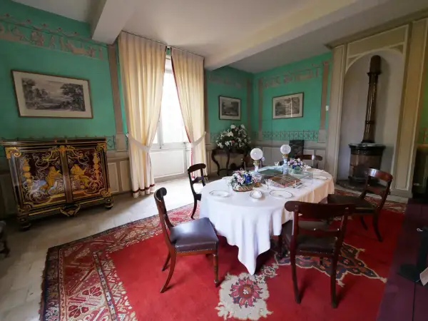 Salle à manger du **château de Saché**, avec une table dressée, un buffet orné et des murs aux motifs décoratifs.