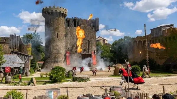 Spectacle de feu et de chevaliers devant le **château du Puy du Fou**. Des flammes jaillissent du donjon, des combattants s'affrontent.
