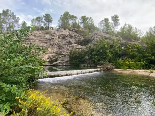 La source du Lez, une cascade artificielle sur une rivière bordée de falaises rocheuses et de végétation luxuriante.