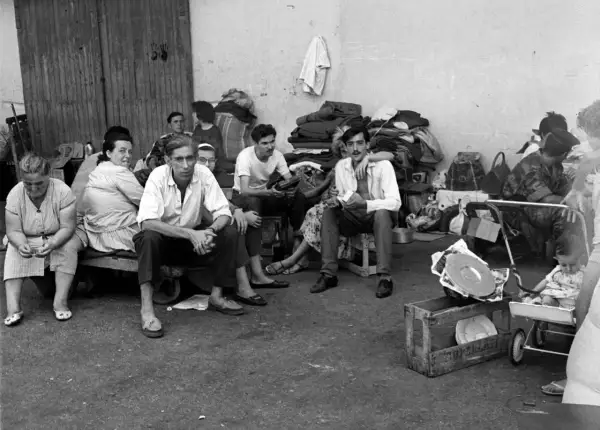 Un groupe de personnes, dont des hommes, des femmes et un bébé, attendent, reflétant le caractère des pieds-noirs dans l'attente.