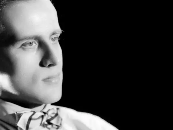 Portrait en noir et blanc d'un homme avec un nœud papillon, regardant sur le côté.