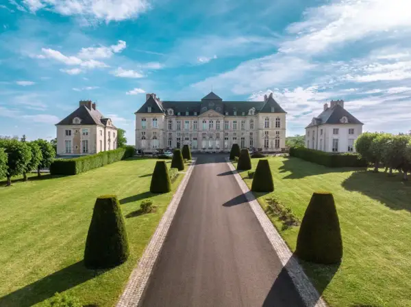 Le majestueux château de Brienne, avec ses ailes symétriques et son allée bordée de topiaires, sous un ciel bleu éclatant.