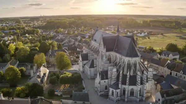 Vue aérienne de la basilique de Cléry-Saint-André au coucher du soleil, baignant le village et ses toits dans une lumière dorée.