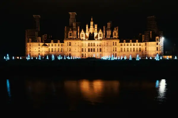 Un château illuminé la nuit, bordé de sapins bleus scintillants, évoque la magie de Noël aux Châteaux de la Loire.