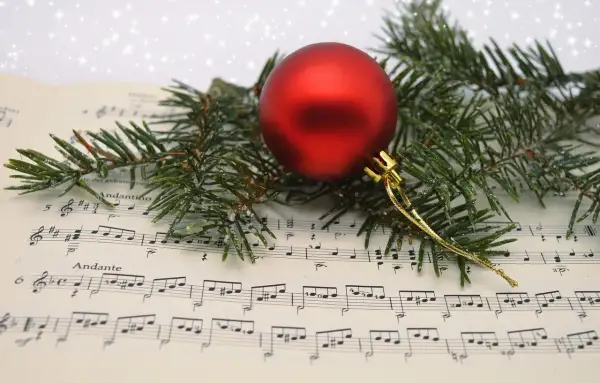 Boule rouge sur partition de "Minuit Chrétien", entourée de branches de sapin givrées. La musique de Noël prend vie.